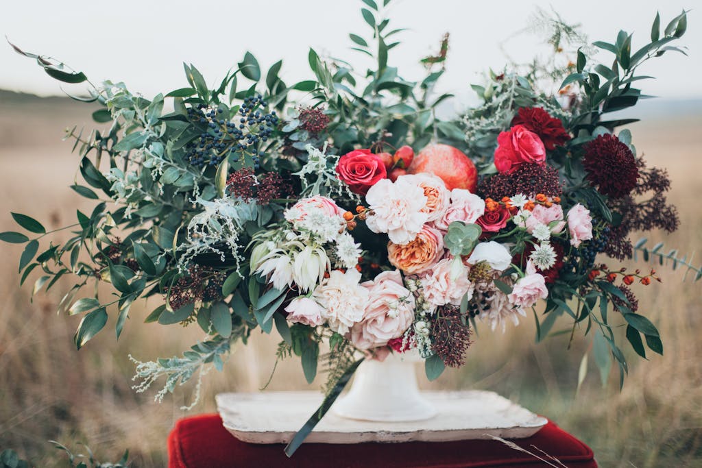 A beautiful floral bouquet with roses and foliage in a white vase outdoors.