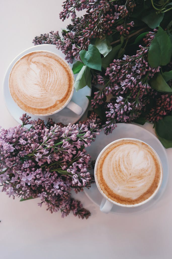 Artistic latte art surrounded by blooming lilac flowers creates a cozy, aesthetic vibe.