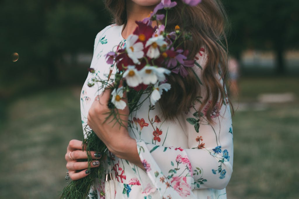 Young woman in floral dress holding a colorful bouquet outdoors, exuding a springtime vibe.